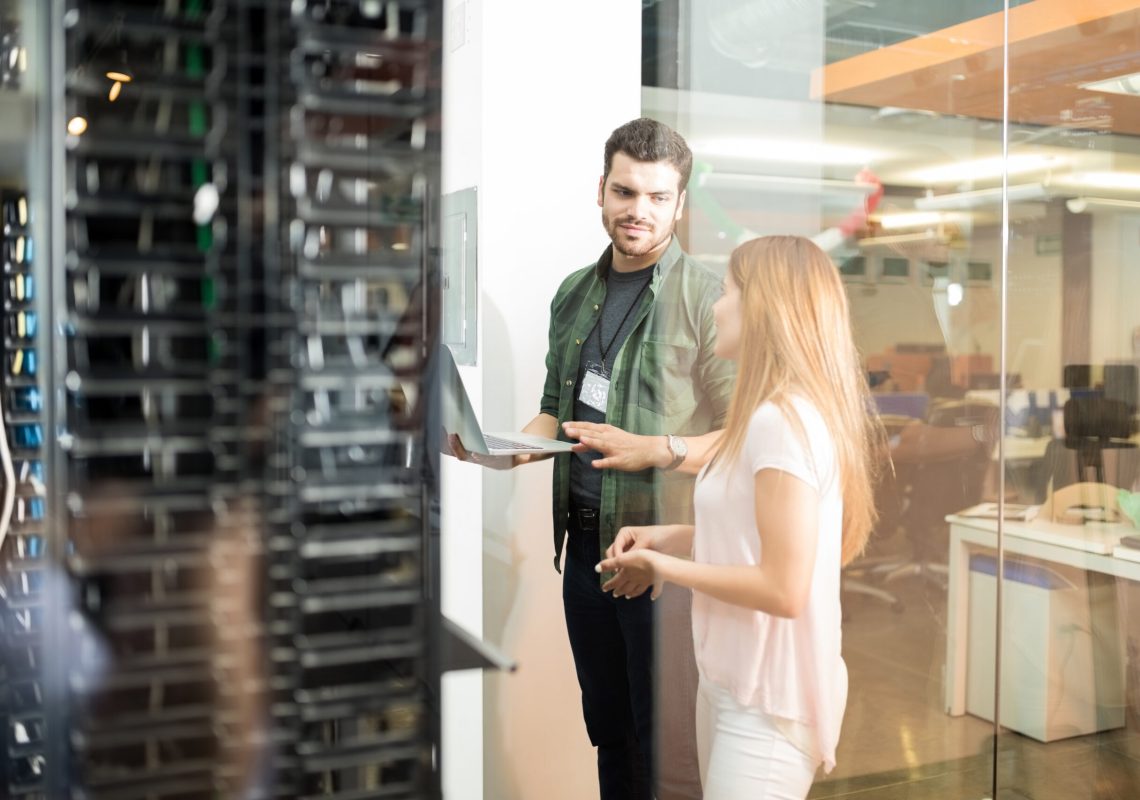 Two business people standing in server room with laptop and discussing