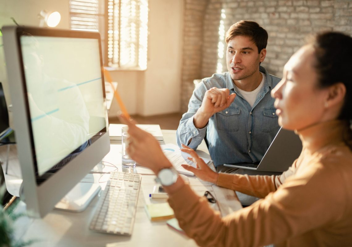 Freelance workers communicating while working together on desktop PC in the office.